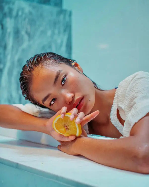 A woman dripping wet from bathing in the swimming pool, grabbing an orange slice in her right palm.